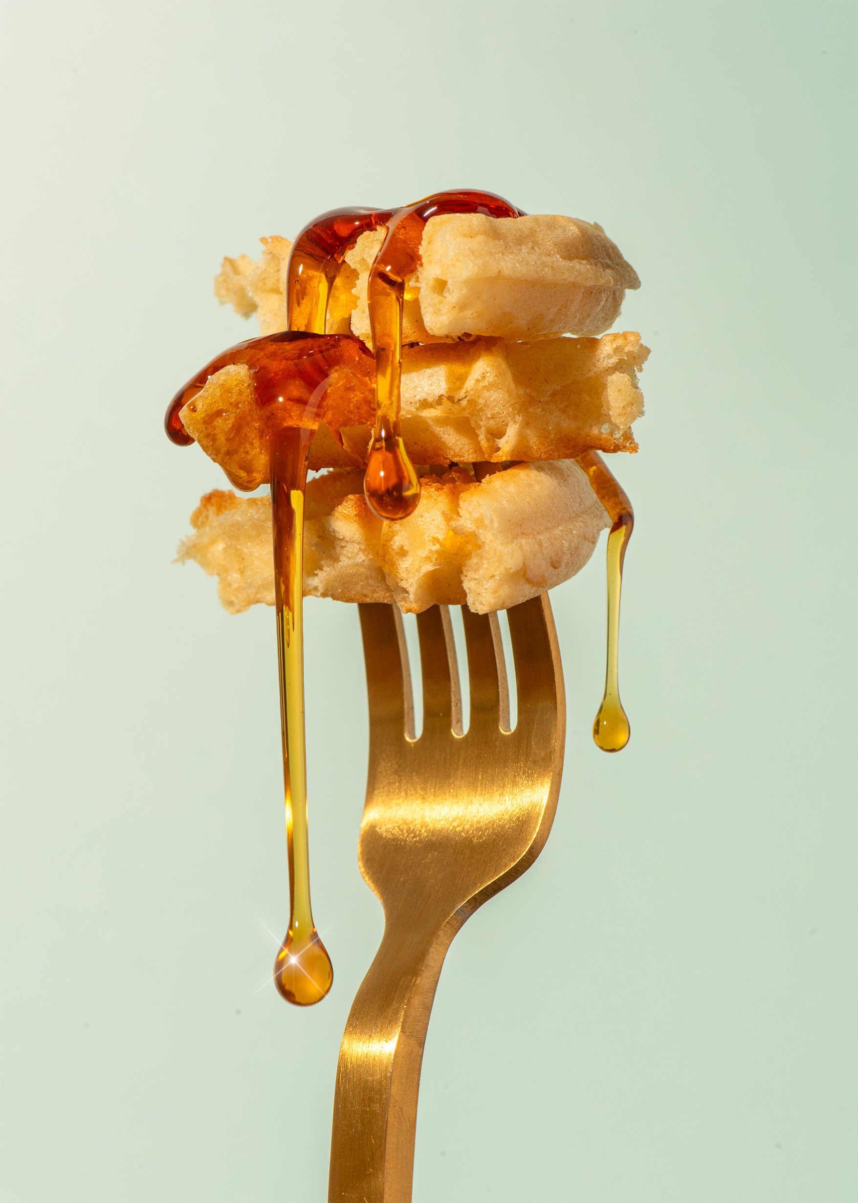 Maple syrup dripping off waffles on gold fork