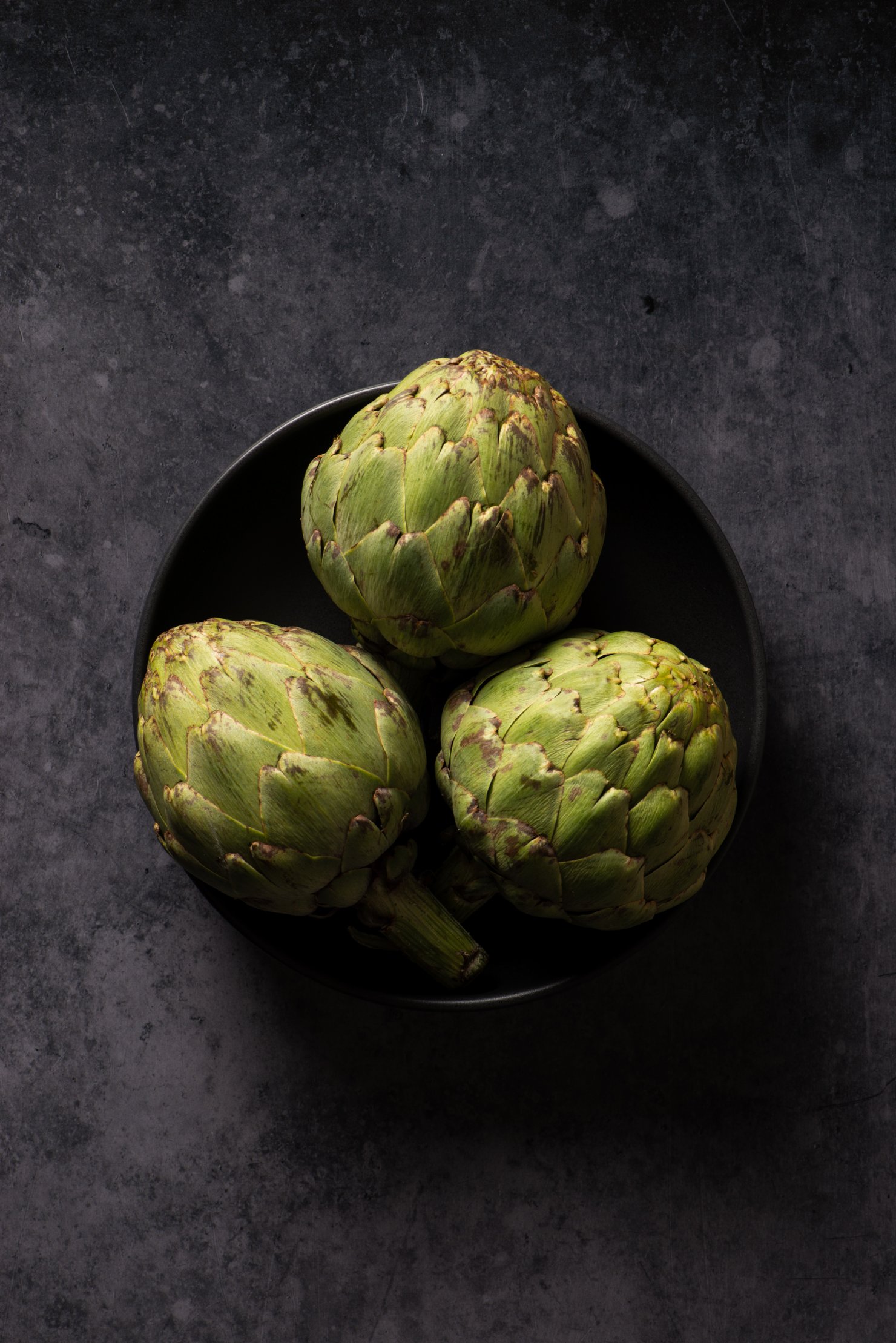 Bowl of fresh artichokes in dark and moody setting