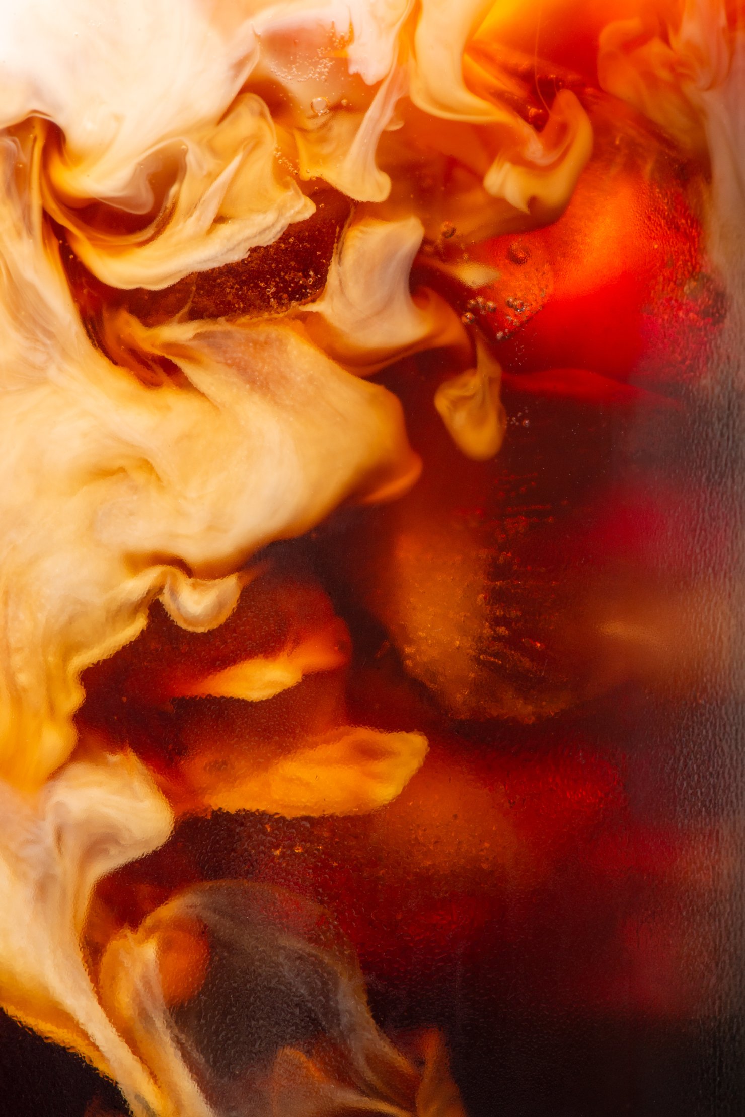 Oat milk mixing with cold brew coffee and ice close up