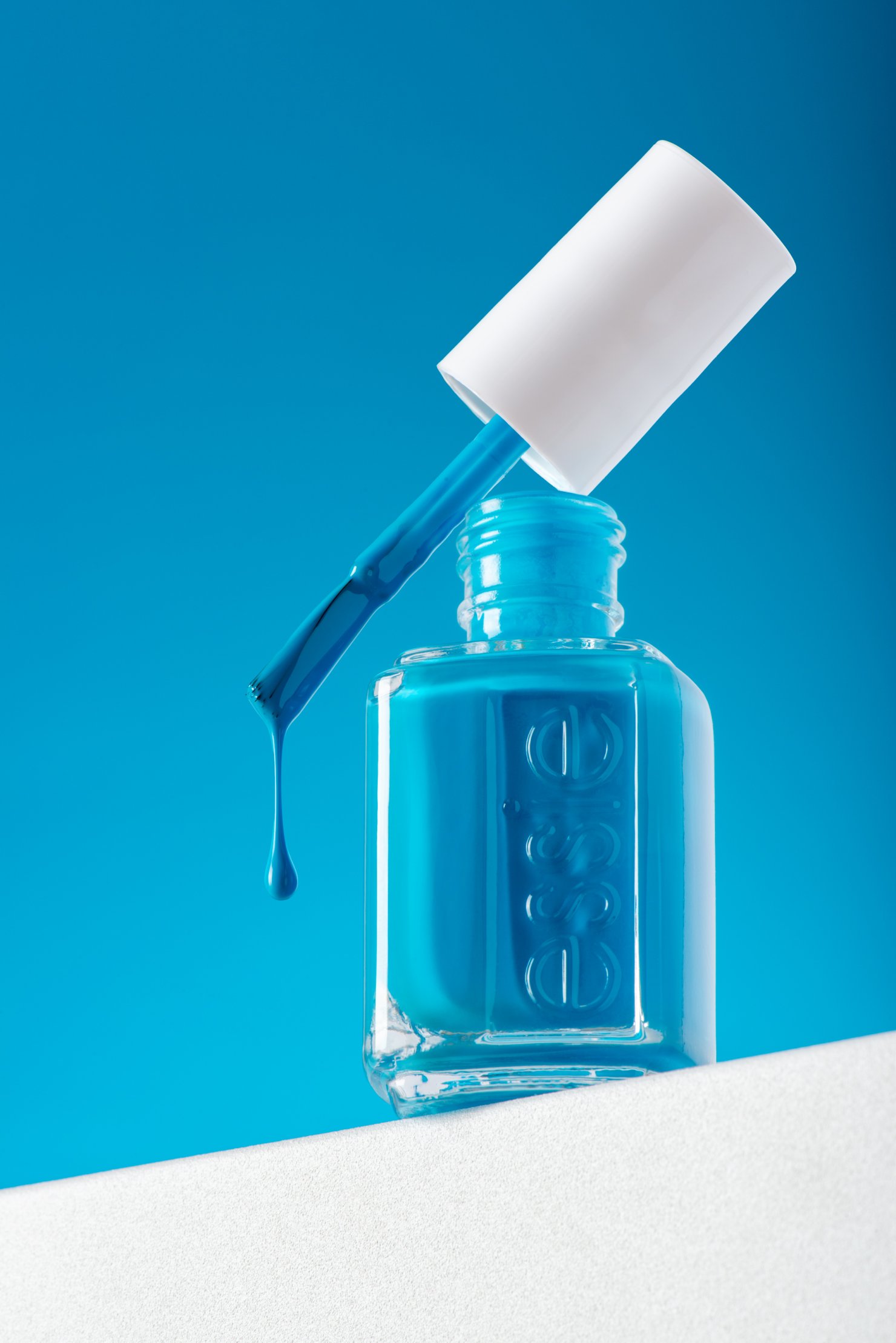 Hero product photography of blue nail polish bottle close up with dramatic drop from brush in motion