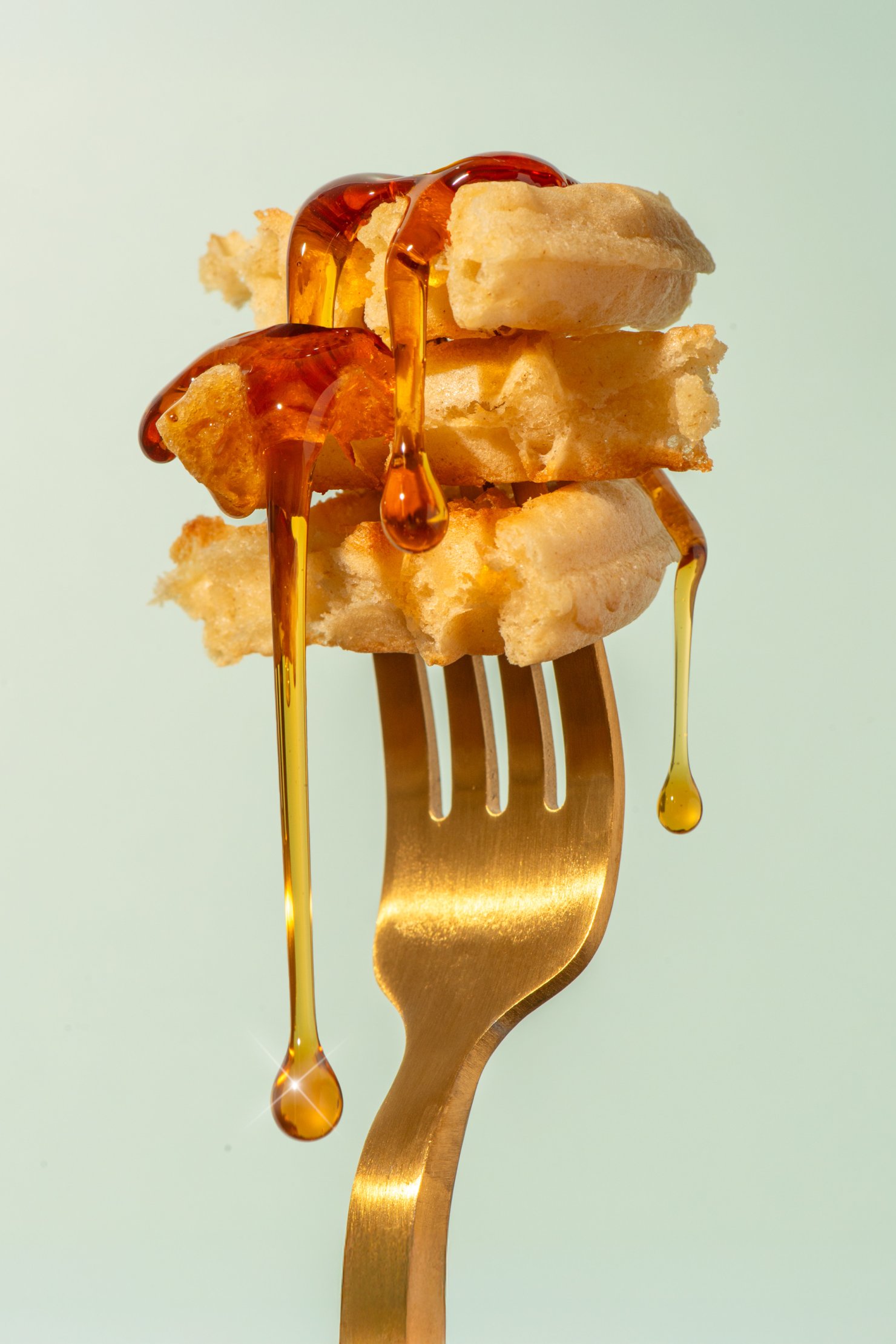 Modern and commercial image of amber coloured maple syrup dripping from waffles on gold fork