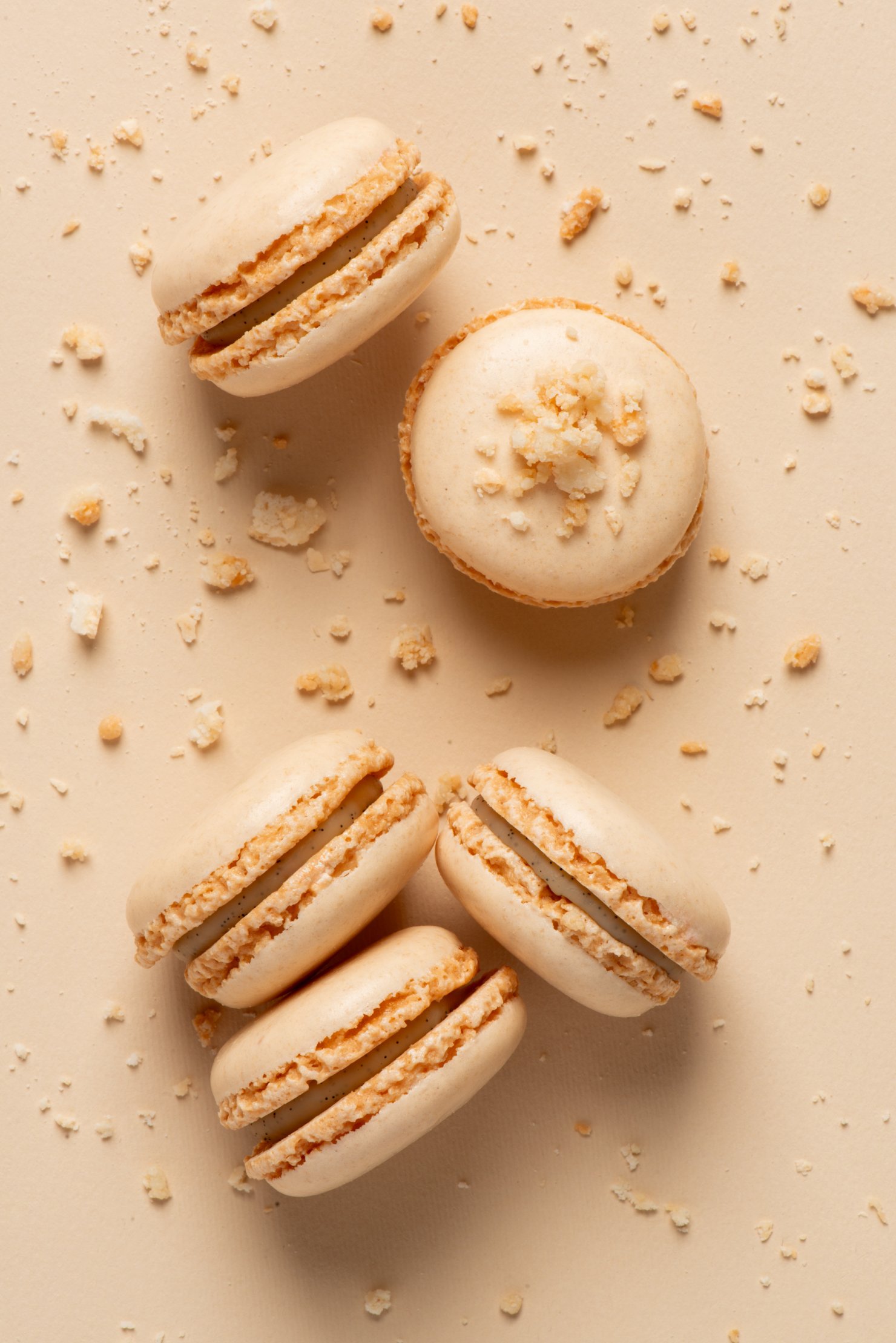 Five light pink macaroons on same colour background with crumbs