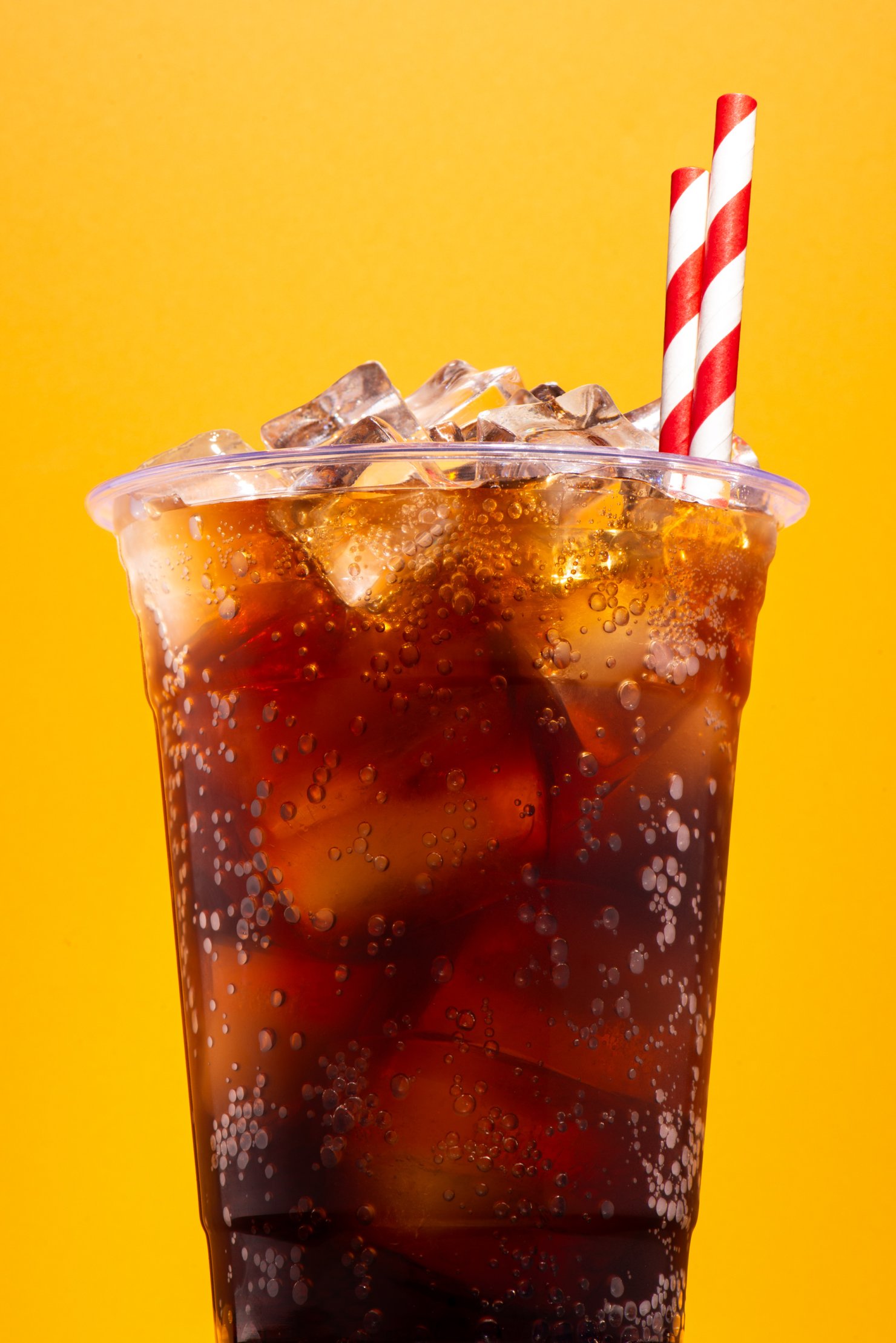 Commercial photography image of dark soda in a plastic cup with red paper straws
