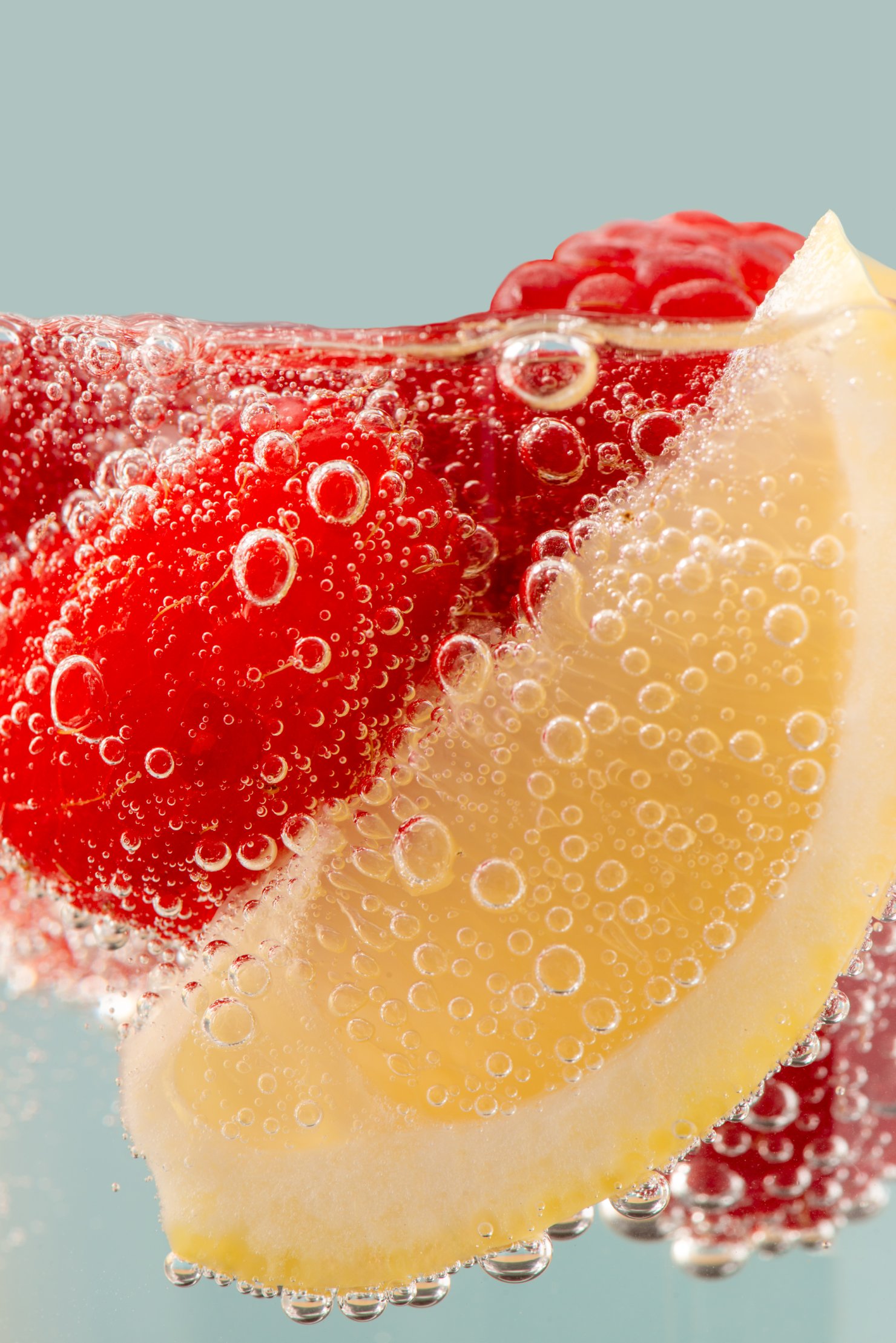 Raspberry and lemon in soda water close up with fizz bubbles