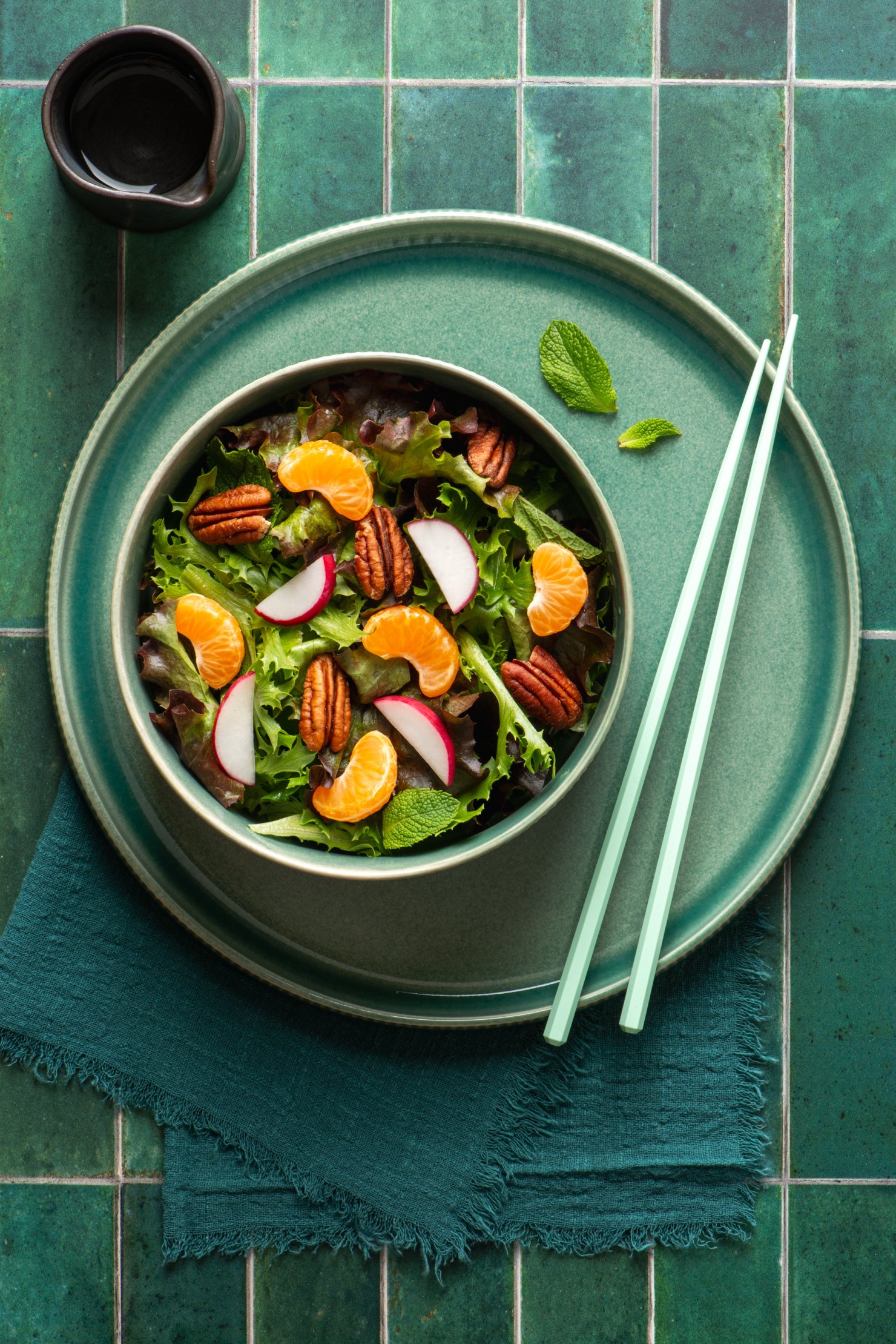 Food photography of salad with pecans, clementines and radish in turquoise bowl on turquoise tile background