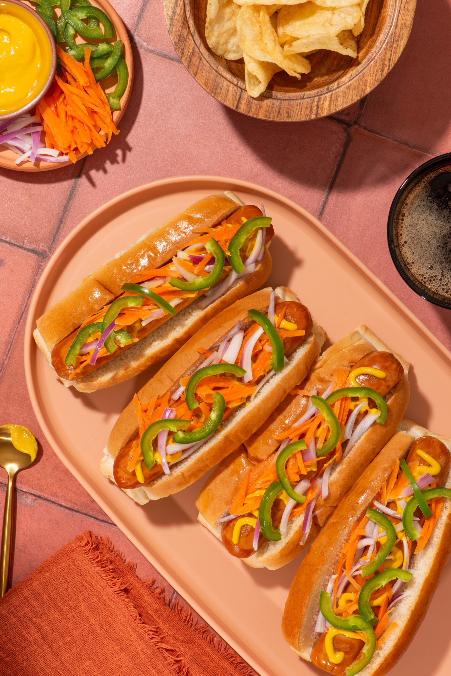 Commercial advertising photograph of four veggie dogs in platter topped with jalapeño, carrot, red onion and mustard.