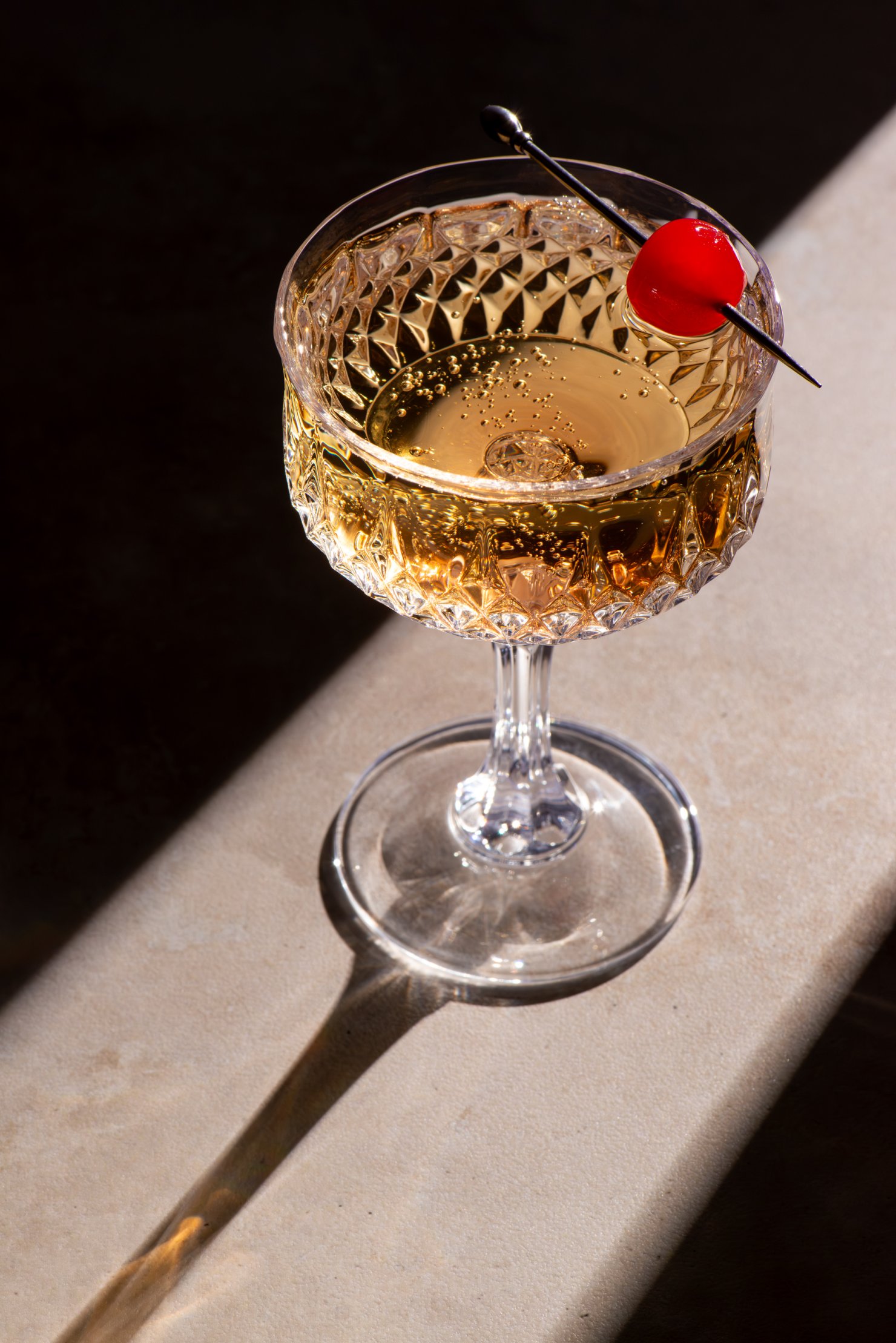 Commercial photography of vintage champagne glass with red cherry and moody elegant lighting by Mel Discepola